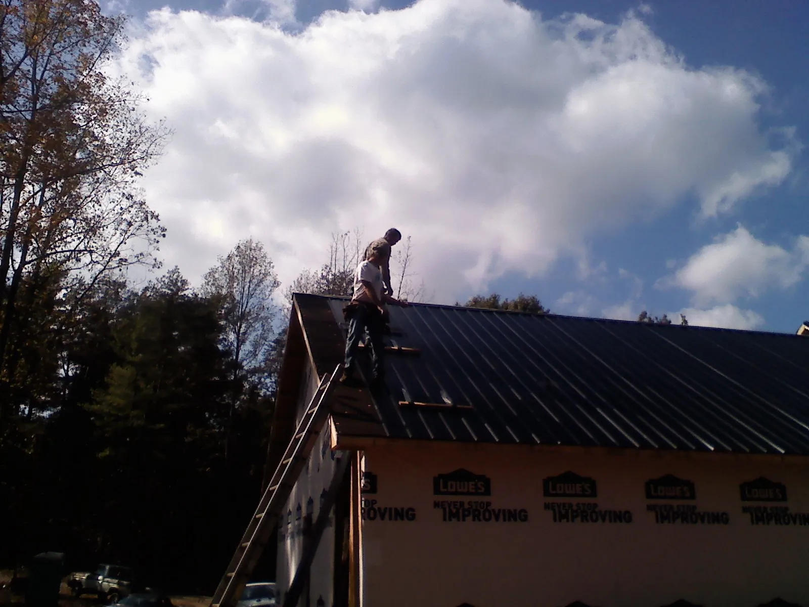 Roofer fastening dark metal panels high against a cloudy sky, from a Roof Inspection job in Waterford